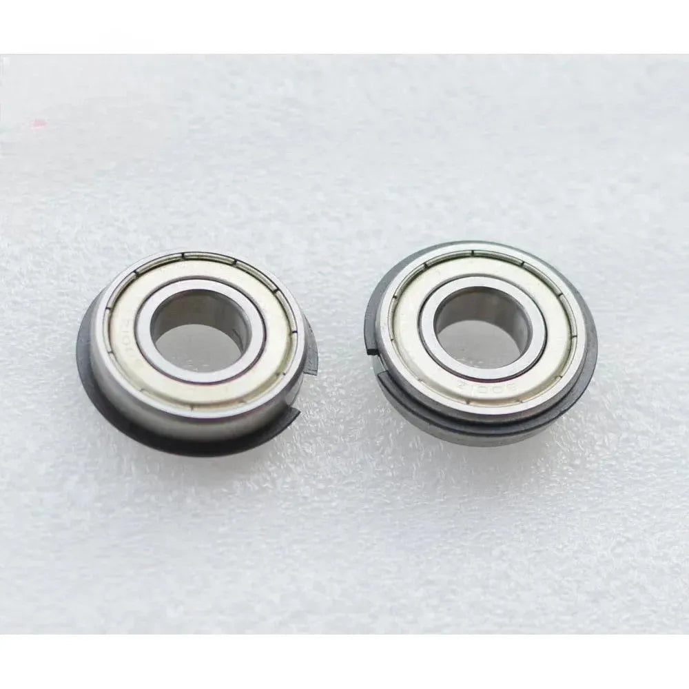 Two Canon IR5075 LOWER BERING metal components are side by side on a textured surface. Each has a central hole, metallic outer rings with grooves, and visible seams around the edge. Brand: Canon.