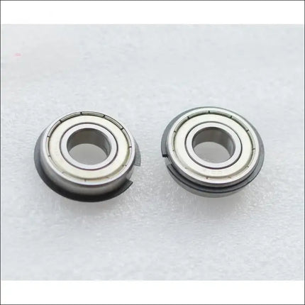 Two Canon IR5075 LOWER BERING metal components are side by side on a textured surface. Each has a central hole, metallic outer rings with grooves, and visible seams around the edge. Brand: Canon.